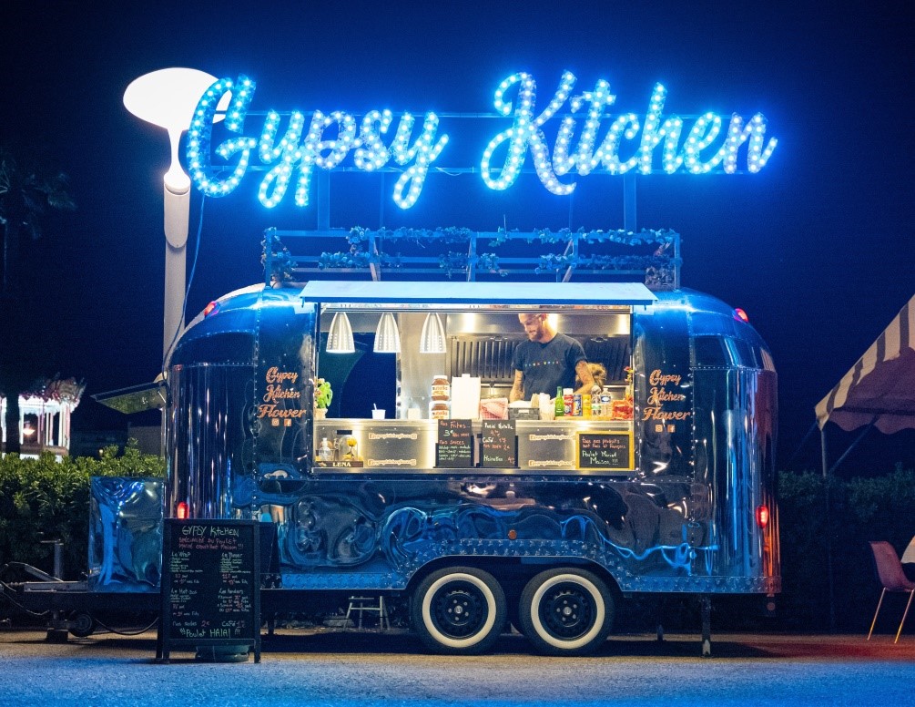 A food truck is parked in the street, lit up in blue, with a sign in front of it with a menu