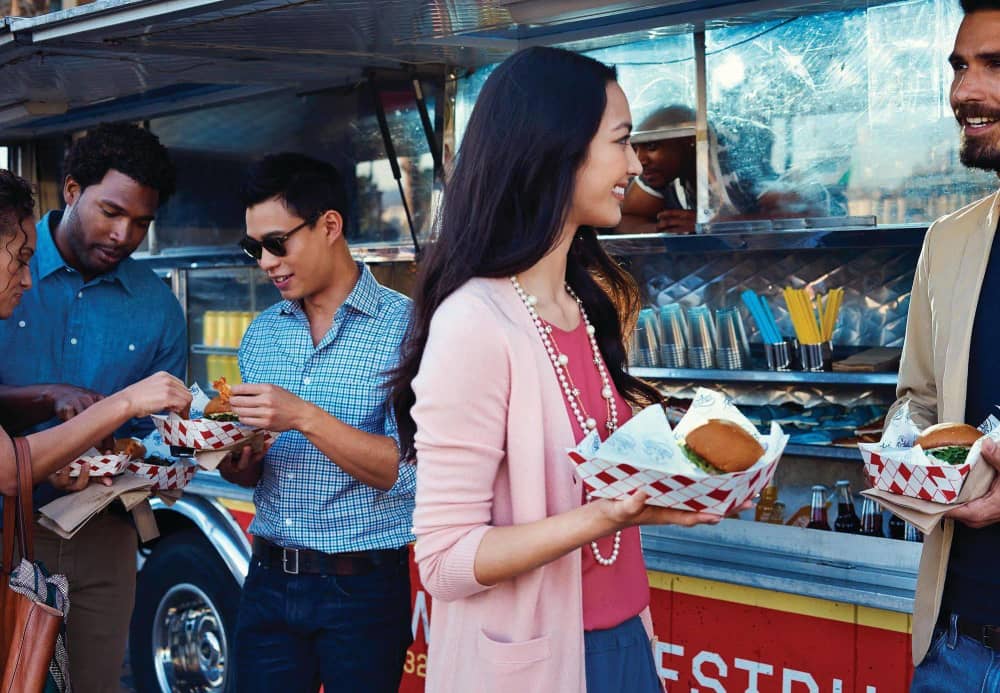 Four people eating free meals in front of a food truck and chatting