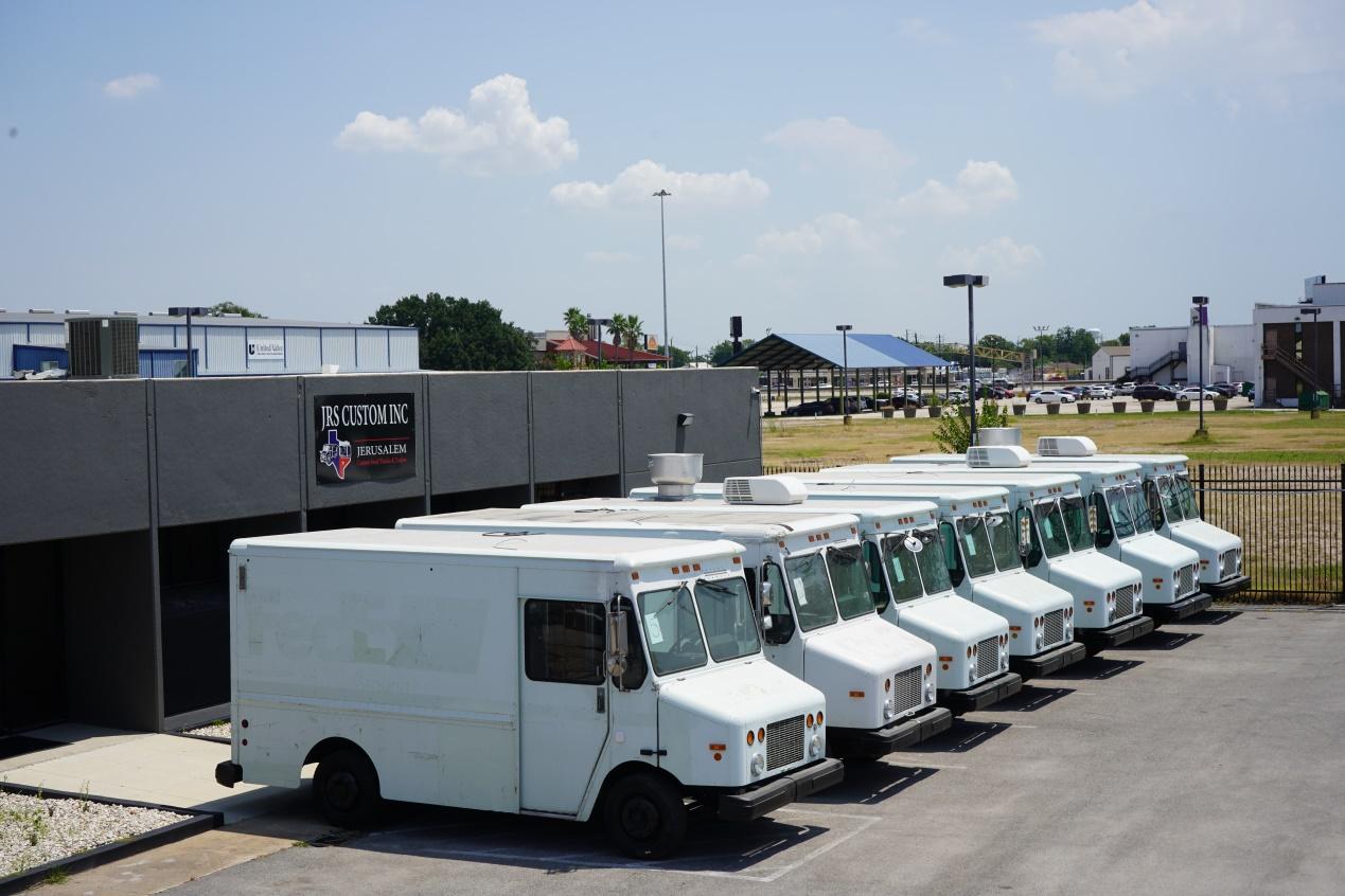 Seven white food trucks made by Jerusalem Company line up in front of Jerusalem Custom Food Truck and Trailer Company building in Houston