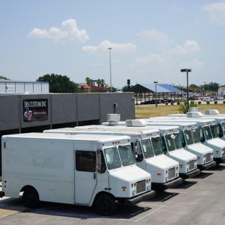 Seven white food trucks made by Jerusalem Company line up in front of Jerusalem Custom Food Truck and Trailer Company building in Houston