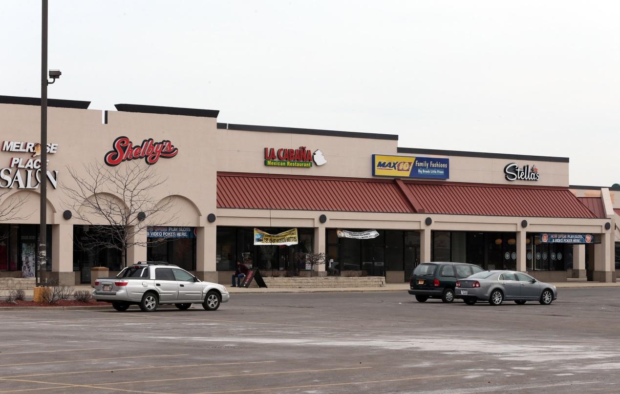 A street containing a series of strip malls with three cars in front of them