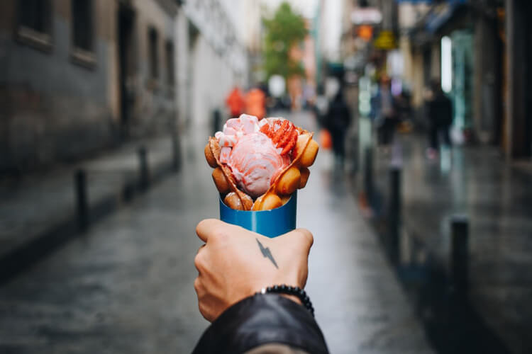 A person carrying a cup of ice cream and sweets on a beautiful street