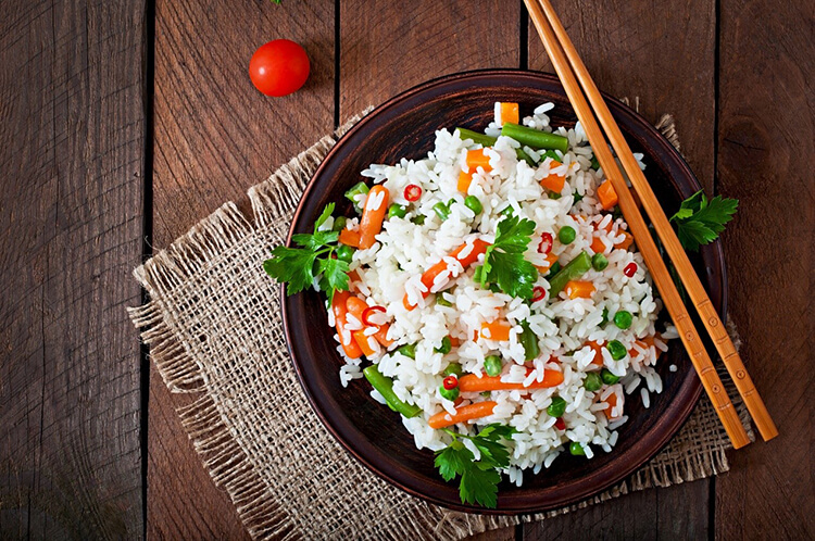 Rice with carrots and vegetables in a black plate with chopsticks