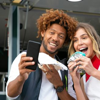 two people taking a selfie in front of a food truck posing with the food they just purchased