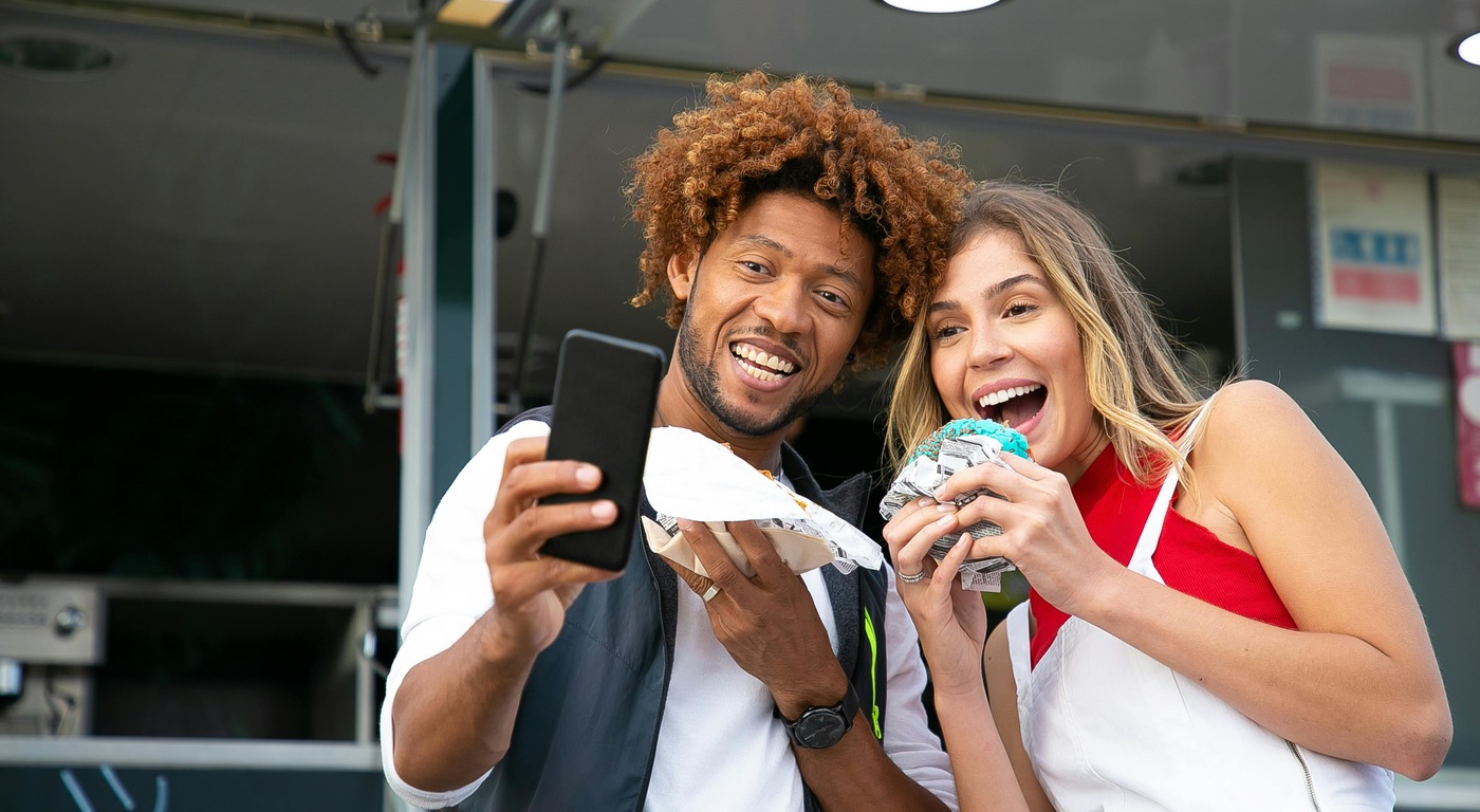 two people taking a selfie in front of a food truck posing with the food they just purchased