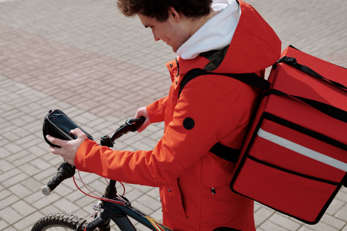 Food delivery courier on a bicycle checking a smartphone while carrying an insulated delivery bag