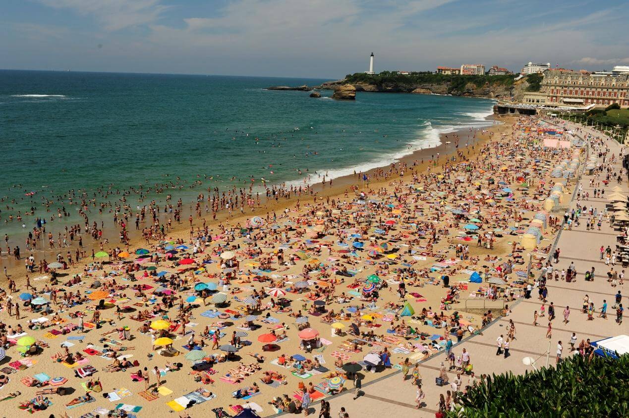 A sandy beach on which dozens of tourists sit