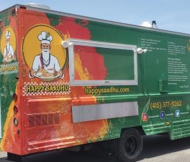 Happy Saadhu South Indian food truck with a vibrant green and orange wrap featuring a sage chef mascot holding a thali plate, mission and sourcing statements, website, phone number, social media handles, and a "We Cater" callout