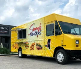 Sammy's Burgers food truck wrapped in a bright yellow sunburst design with large food illustrations including a burger and wings, open service window, parked outside JRS Custom Inc