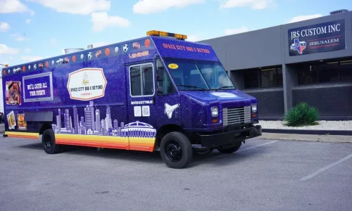 Three-quarter front view of the Space City BBQ and Beyond food truck with a deep purple galaxy wrap, Houston skyline, sports ball roof border, space shuttle graphic, and catering messaging