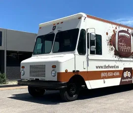 Tamela's Tailgate Treats food truck with a white and brown wrap featuring a football graphic, the tagline "Faith, Family, Food, Football," website, and phone number, parked outside JRS Custom Inc