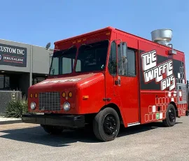 Bright red The Waffle Bus food truck with bold black and white branding and a geometric pattern along the lower body, parked outside JRS Custom Inc in Texas