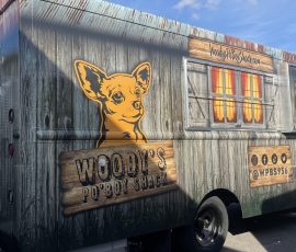 Woody's Po'Boy Shack food truck with a rustic weathered wood plank wrap featuring a Chihuahua mascot illustration, barn window graphic, catering callout, social media handles, phone number, and diamond-plate exterior storage compartment