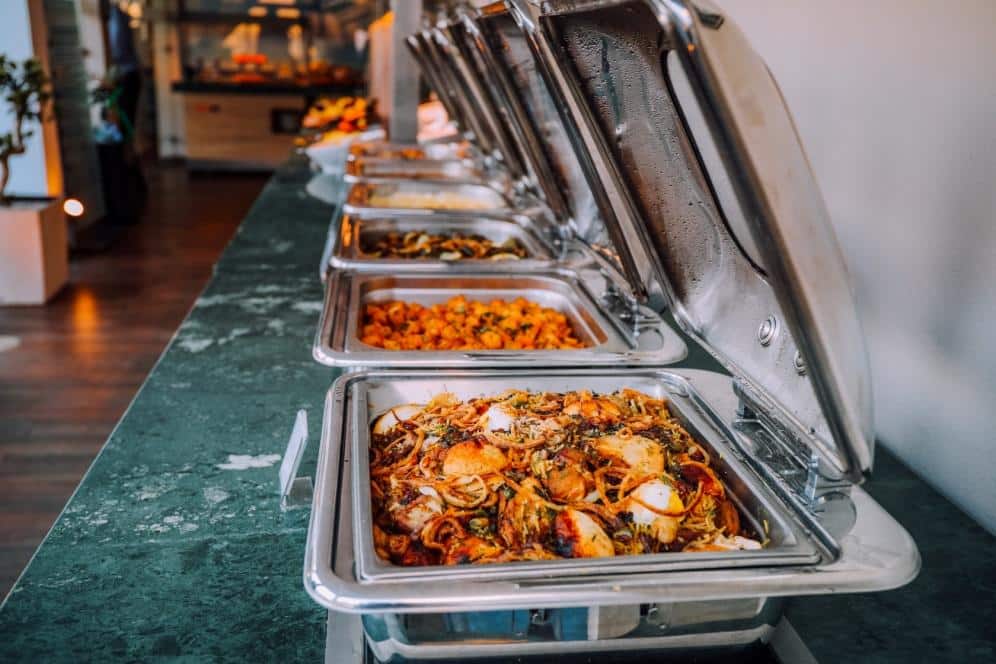 Row of stainless steel chafing dishes filled with food at a catering buffet setup