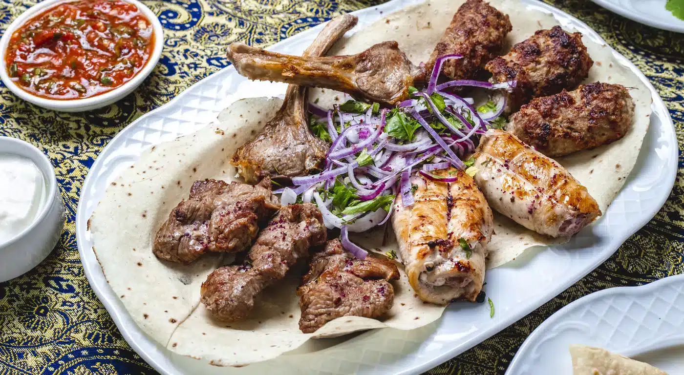 Mixed halal grilled meat platter with lamb chops, chicken, kofta, red onion, and flatbread served with dipping sauces