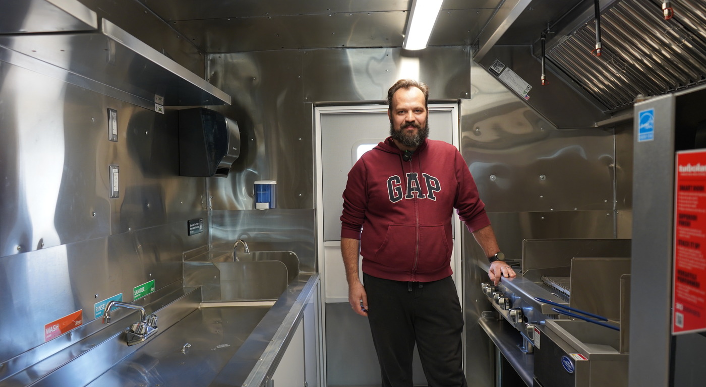 Food truck owner standing inside his custom built stainless steel kitchen with three-compartment sink and commercial cooking equipment