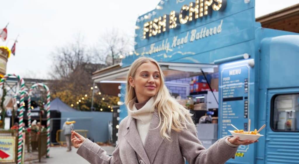 Customer enjoying fish and chips from a food truck at an outdoor market event