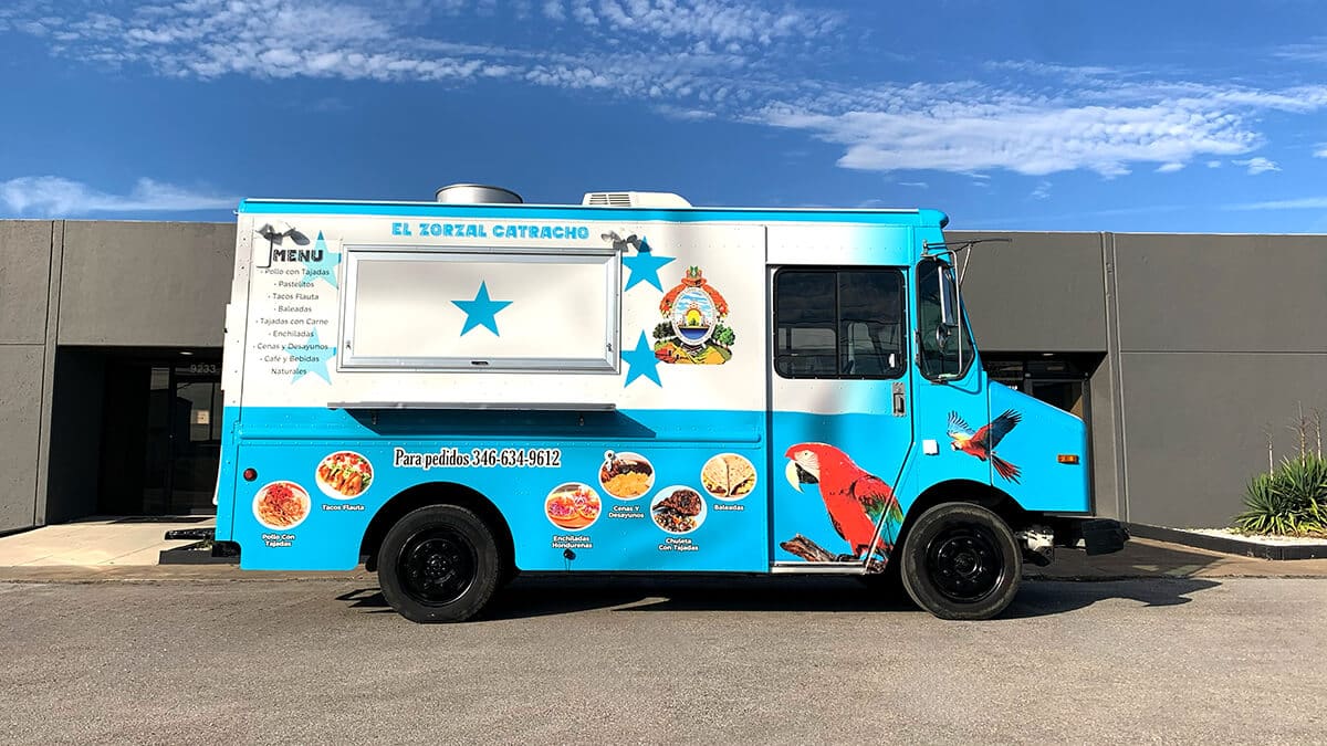 El Zorzal Catracho Honduran food truck with a wrap styled after the Honduran flag featuring blue and white colors, five stars, the national coat of arms, a scarlet macaw illustration, circular menu food photos, and a Spanish menu listing along the side