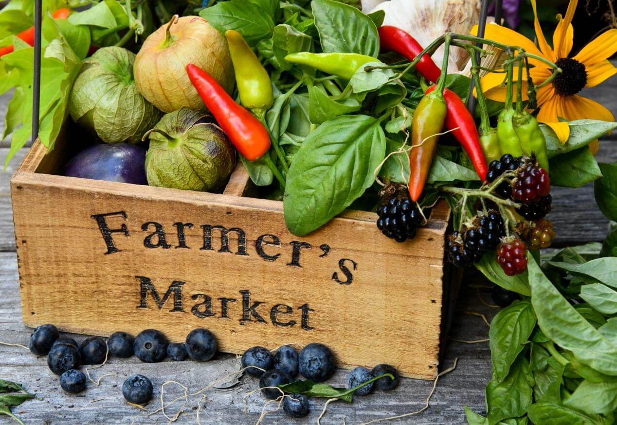 Wooden box labeled Farmers Market The box contains green and red peppers, cranberries, yellow roses and vegetables