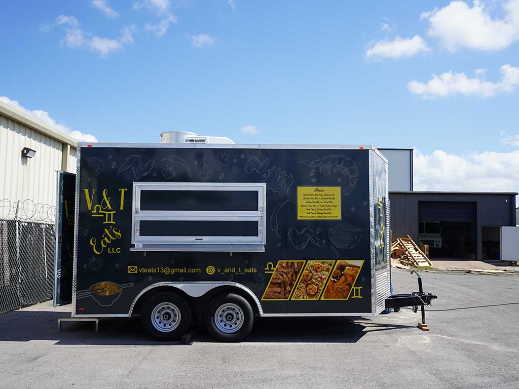 V&T Eats LLC food trailer with a dark wrap featuring hand-drawn seafood illustrations, gold branding, menu board, food photos, and contact details, parked in an industrial lot