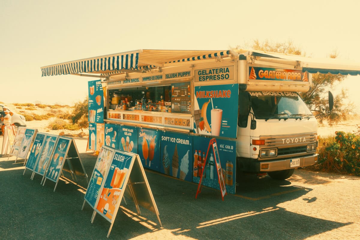 Ice cream and gelato food truck with striped awning extended and menu boards displayed in a sunny outdoor setting