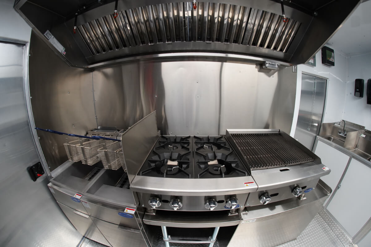 Custom food truck cooking station with commercial fryer, six-burner range, charbroiler, and stainless steel ventilation hood