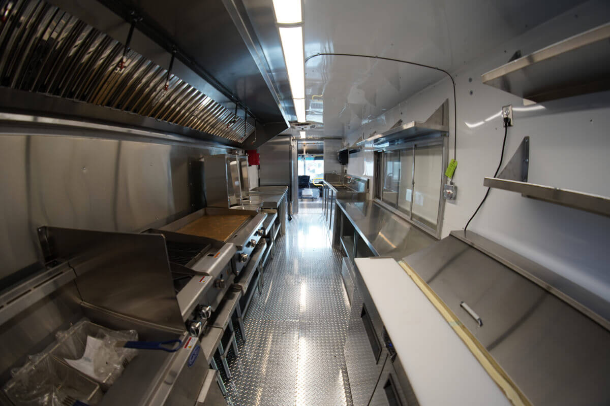 Interior of a custom food truck build by JRS Custom Food Trucks and Trailers showing stainless steel commercial kitchen equipment, diamond plate flooring, and ventilation hood