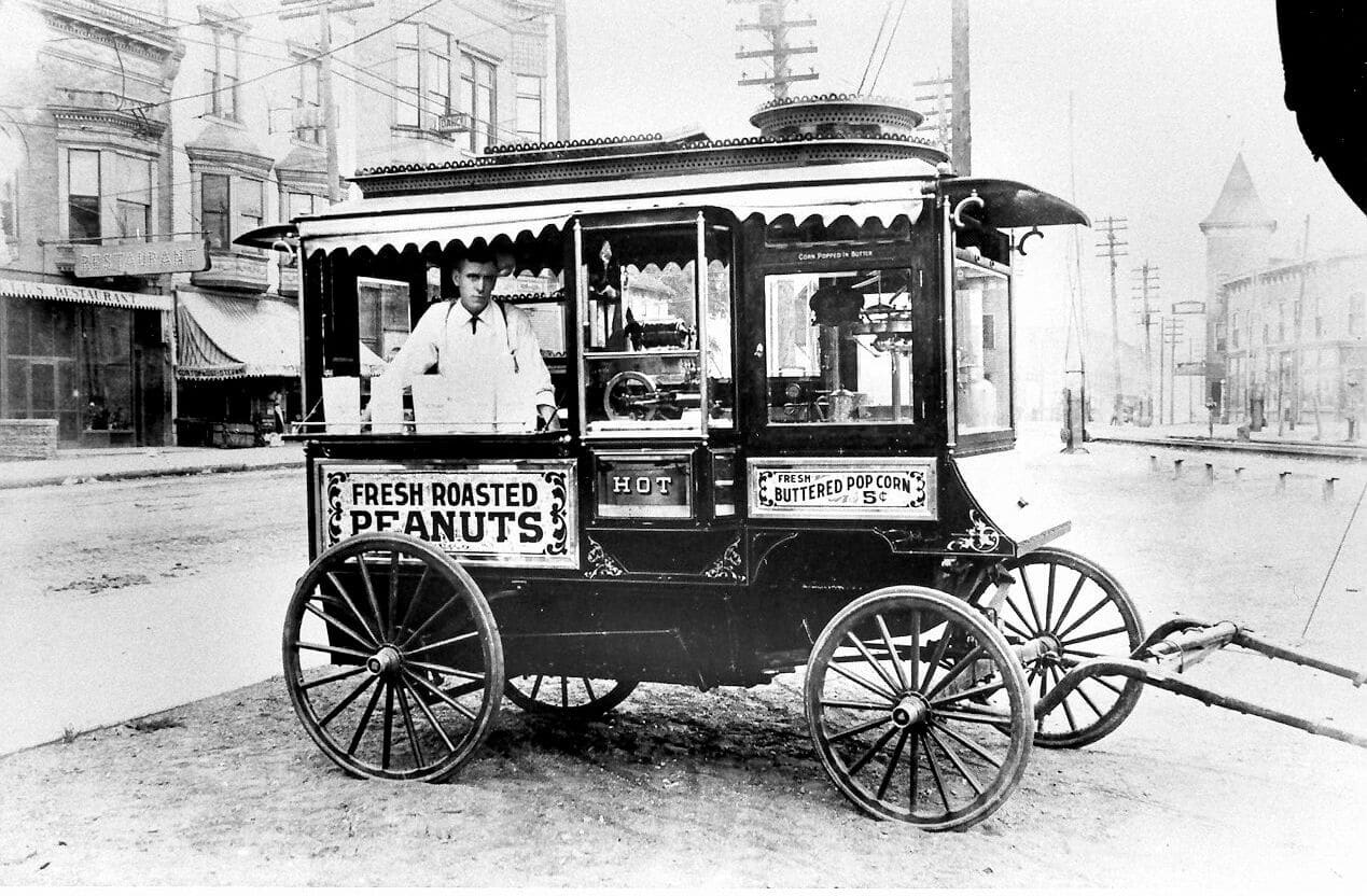 Vintage black and white photograph of an early 1900s street food cart selling fresh roasted peanuts and buttered popcorn
