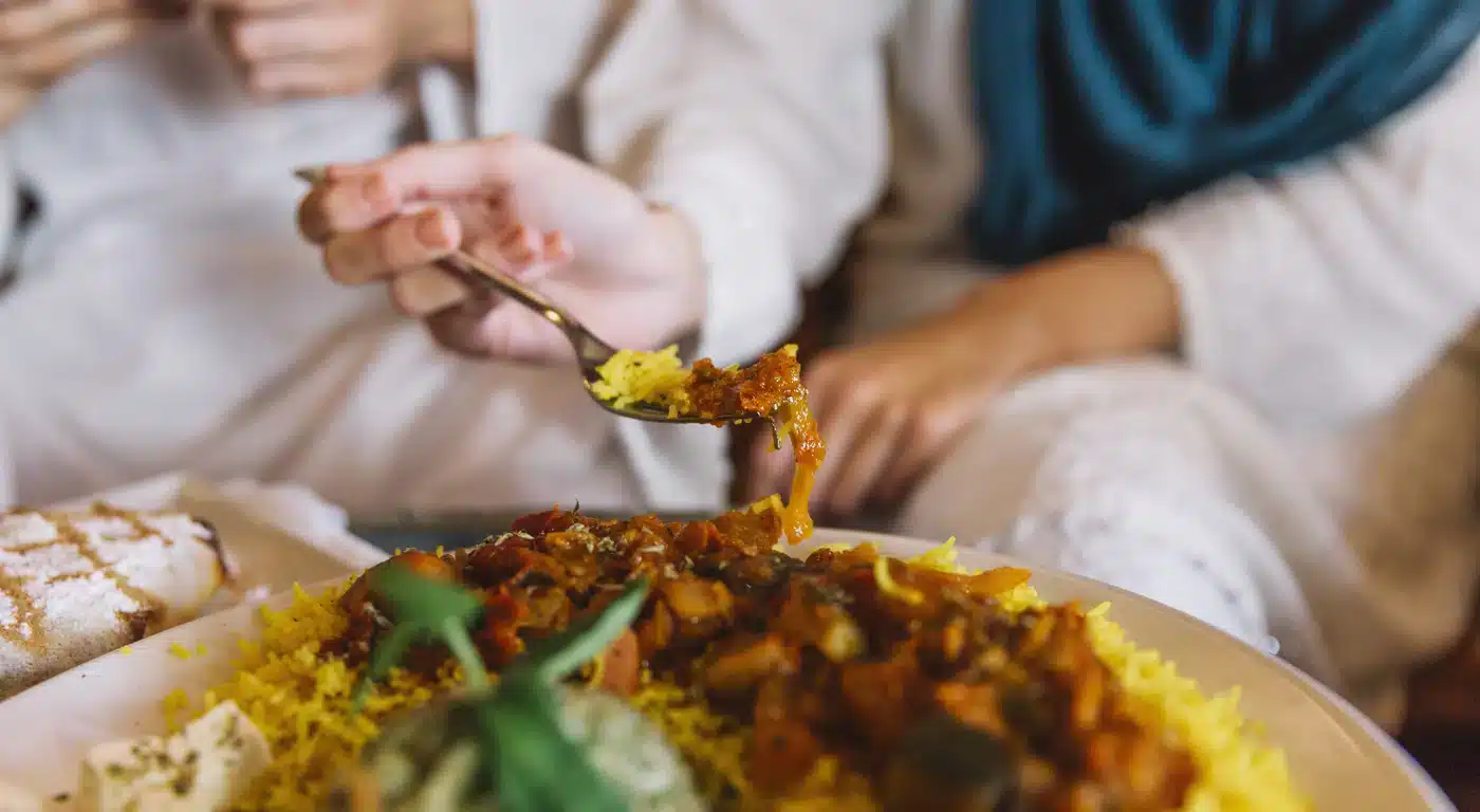 Two people sharing a plate of saffron rice and spiced meat at a halal restaurant