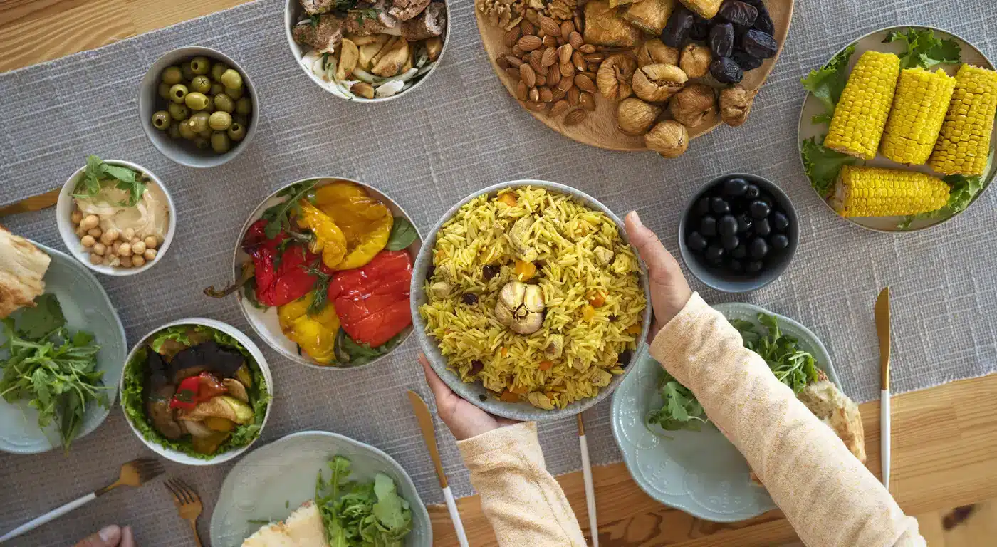 Overhead view of a halal spread with saffron rice, roasted peppers, hummus, olives, dates, nuts, and grilled corn
