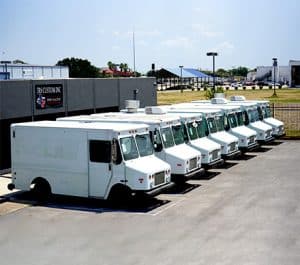 A row of eight white step van food trucks lined up in the lot outside JRS Custom Inc, the Jerusalem Custom Food Trucks & Trailers fabrication facility in Texas