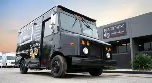 Matte black Kale's Kitchen food truck with branded wrap featuring menu item photos and contact number, parked outside JRS Custom Inc in Texas at dusk