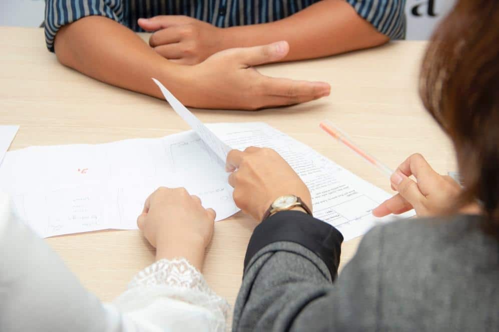 Two people reviewing and discussing official documents and forms at a table