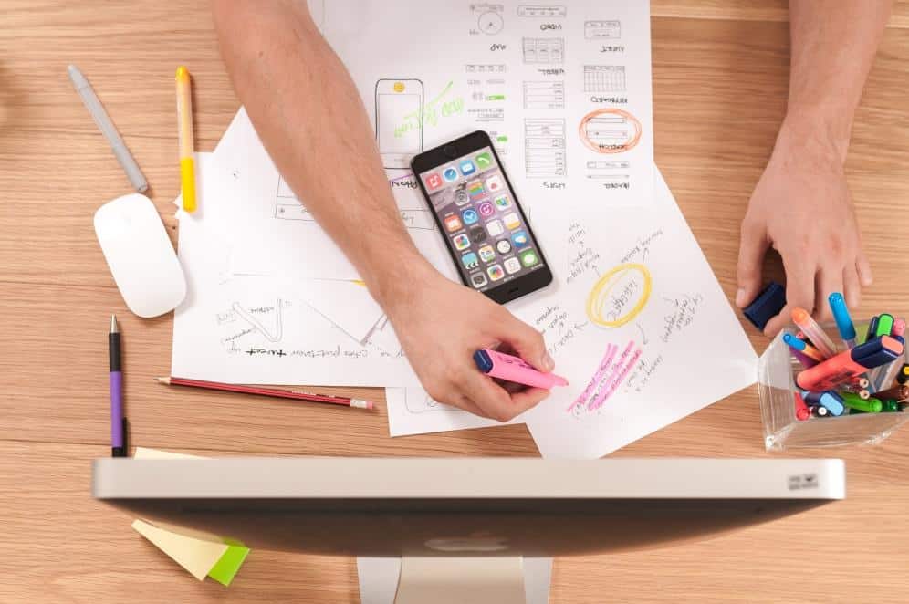 Overhead view of a person planning and sketching ideas on paper with a smartphone, highlighters, and markers on a desk