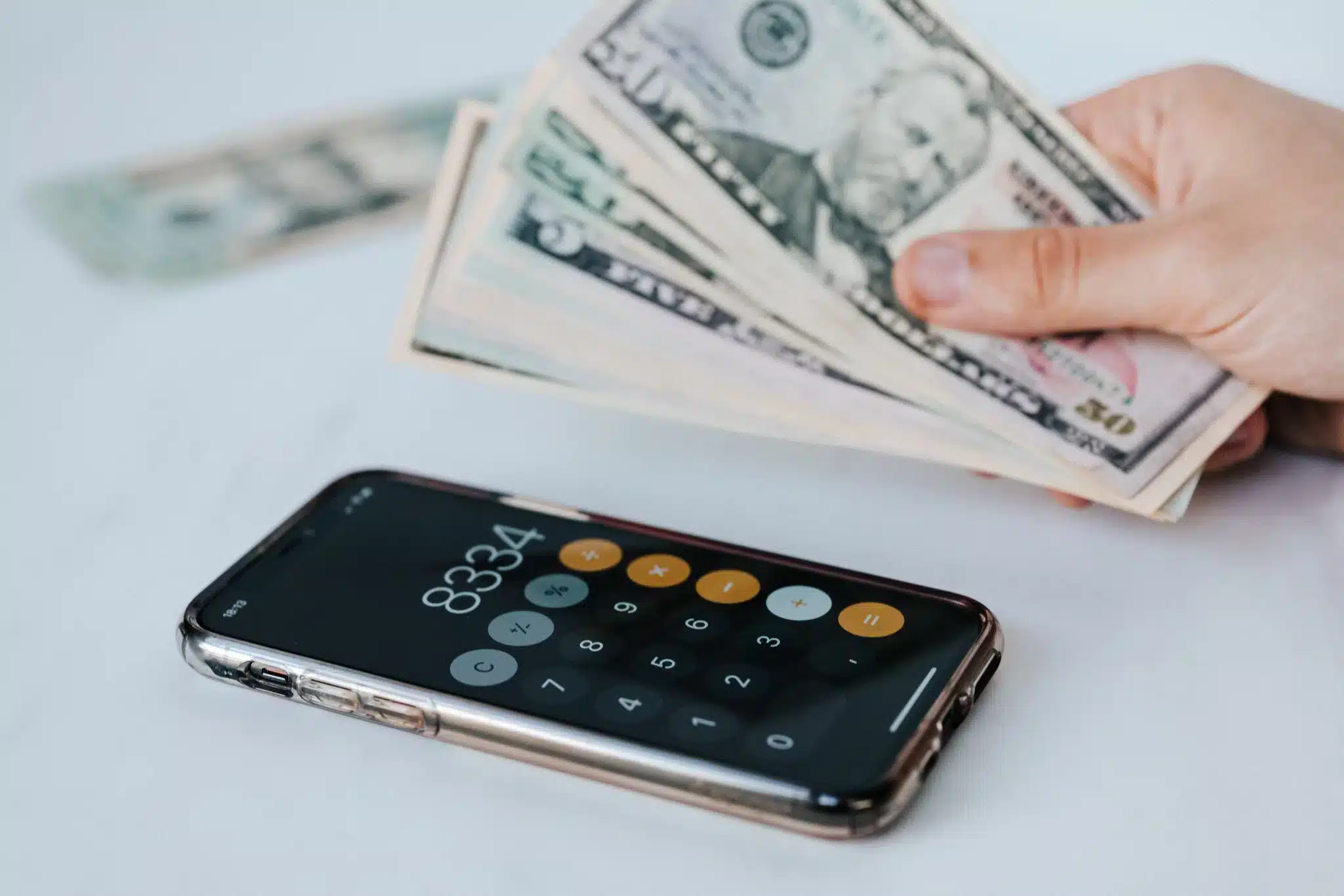 hand holding cash next to a calculator on a white table