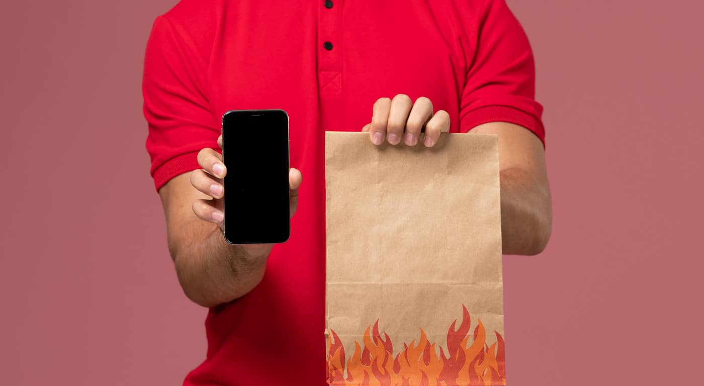 delivery man in a red shirt holding a food order and a mobile phone