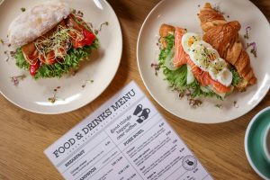 Overhead view of two plated sandwiches beside a printed food and drinks menu on a wooden table