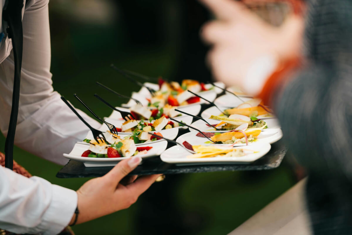 Server carrying a tray of plated appetizers at an outdoor catering event