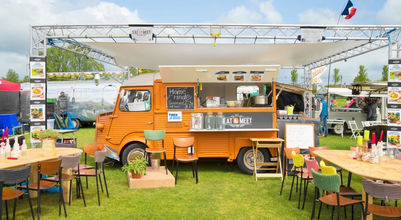 Vintage orange food truck with outdoor seating area set up at a food festival on a sunny day