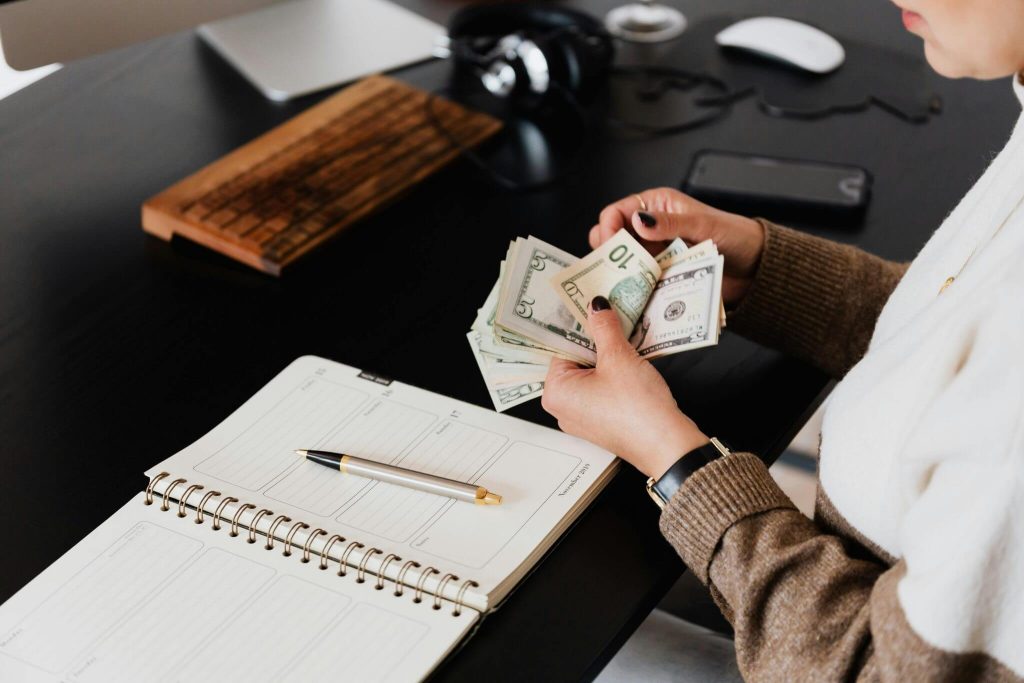 Person counting cash at a desk next to an open planner and pen