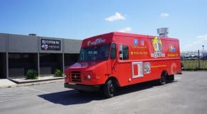 The Taco Man food truck from Berthoud, CO with a bright red wrap featuring a mascot illustration, Colorado logo, social media handles, phone number, and QR code, parked outside JRS Custom Inc in Texas