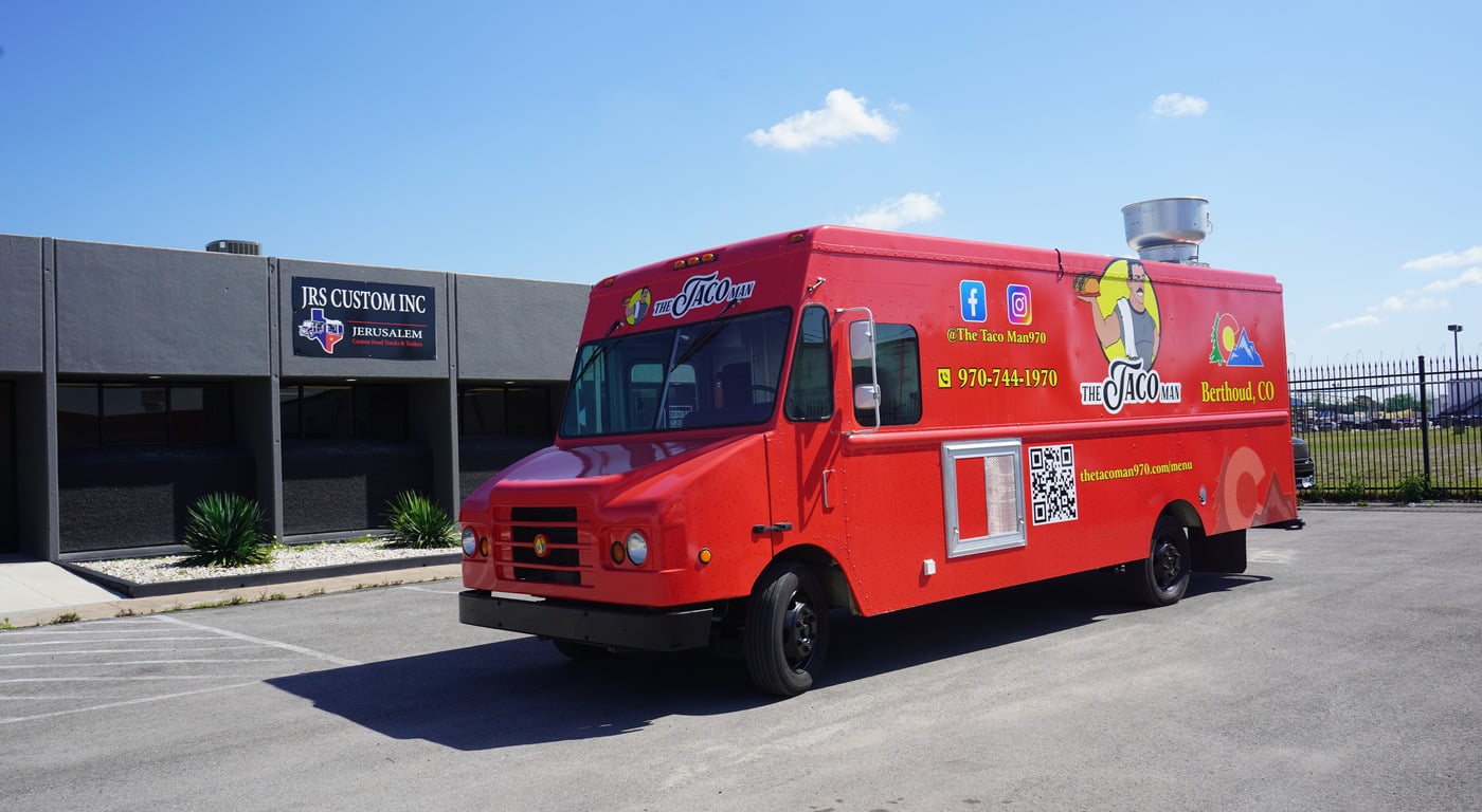 The Taco Man food truck from Berthoud, CO with a bright red wrap featuring a mascot illustration, Colorado logo, social media handles, phone number, and QR code, parked outside JRS Custom Inc in Texas