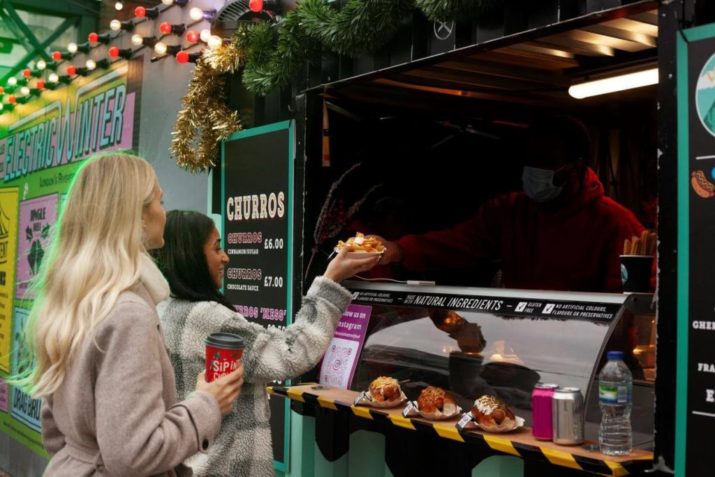 Two girls, one brunette and one blonde, order two meals from a colorful food truck ( Food Truck Customers )